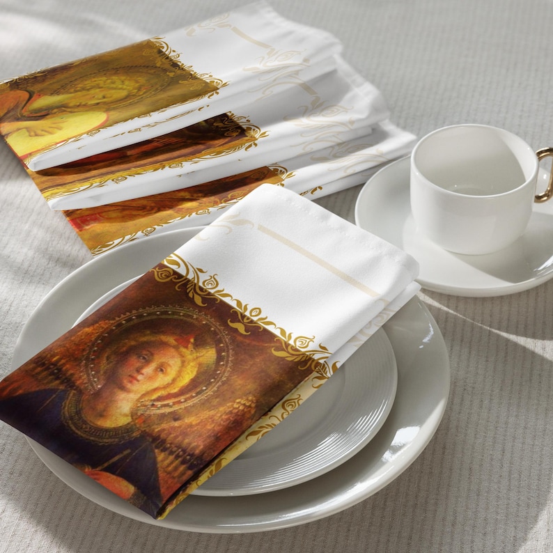 以下が含まれることがあります： ルネサンス様式の天使の絵が描かれた白い布ナプキン。金色のアクセントと装飾的なボーダーが特徴です。ナプキンは白いお皿の上に重ねられ、背景には白いティーカップとソーサーがあります。