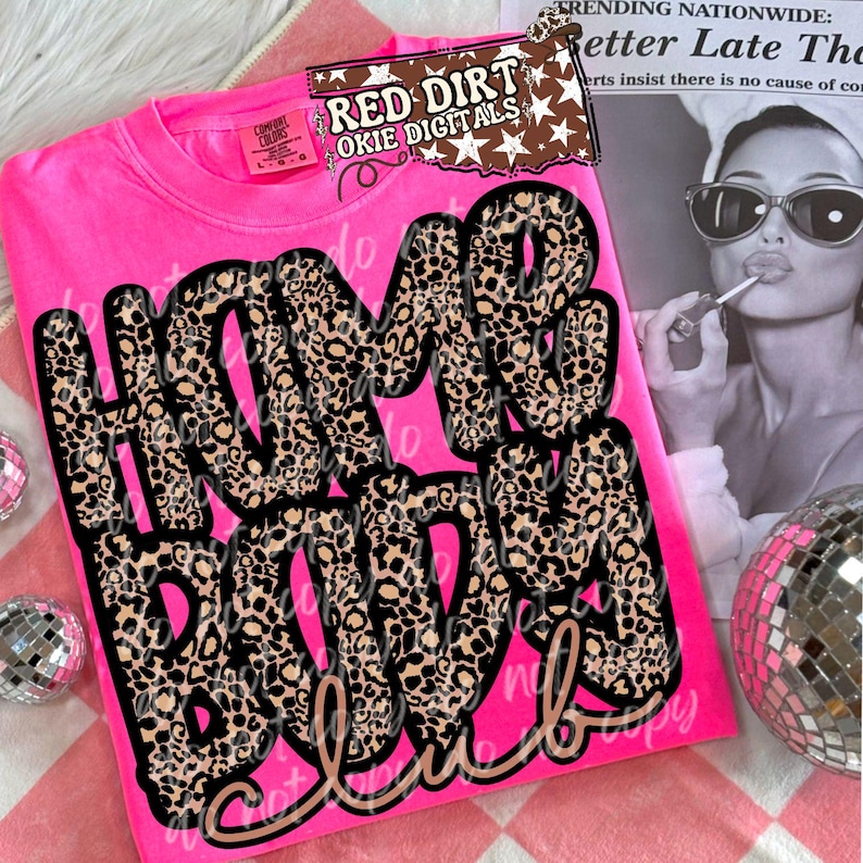 May include: A bright pink t-shirt with the words "HOME BODY CLUB" in a leopard print design. The shirt has a crew neck and short sleeves. The text "RED DIRT OKIE DIGITALS" is in the upper right corner. The shirt is on a pink and white checkered surface.