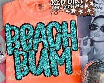 Op de afbeelding: Een oranje t-shirt met de woorden "BEACH BUM" in grote, turquoise luipaardprint letters. Het shirt heeft een ronde hals en korte mouwen. De tekst "RED DIRT OKIE DIGITALS" staat rechtsboven.