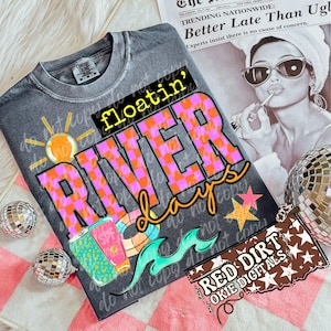 May include: A grey t-shirt with the words "floatin' RIVER days" in a colourful checkered design. The shirt features a sun, sunscreen, and a pool float graphic. A newspaper and disco balls are in the background.
