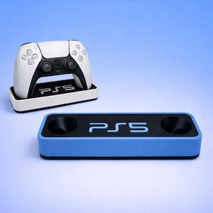 May include: A white and black PS5 controller sits on a white and black stand. Below, a blue and black charging station with the PS5 logo is visible. The items are set against a gradient blue background.
