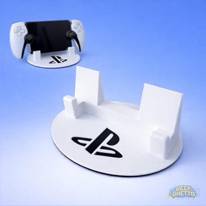 Può includere: Supporto bianco per console di gioco con logo PlayStation nero. Il supporto è progettato per contenere un controller di gioco e un dispositivo mobile. Lo sfondo è una sfumatura di blu.