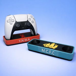 May include: A white and black games controller sits on a red and black base with the text "Y.N.W.A". A second blue and black base features the text "M.C.F.C" and a yellow ship graphic. The items are on a blue background.