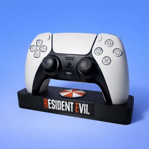 May include: A white and black PlayStation 5 controller rests on a black base. The base features the "Resident Evil" logo and a red and white umbrella logo. The controller has a symmetrical design with buttons and joysticks.