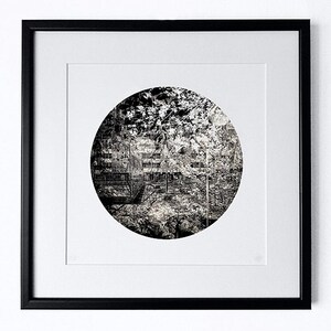 May include: A black and white photograph of a building framed in a black frame. The photograph is in a circle shape and the building is surrounded by trees.