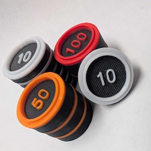 May include: Four 3D printed game tokens with different values. The tokens are black with white, orange, and red accents. The values are 10, 50, 100, and 10.
