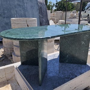 Puede incluir: Una mesa de m&aacute;rmol verde con una tapa ovalada y dos soportes rectangulares. La mesa tiene una superficie pulida y un patr&oacute;n de piedra natural. La mesa mide aproximadamente 152 cm de largo y 76 cm de ancho.