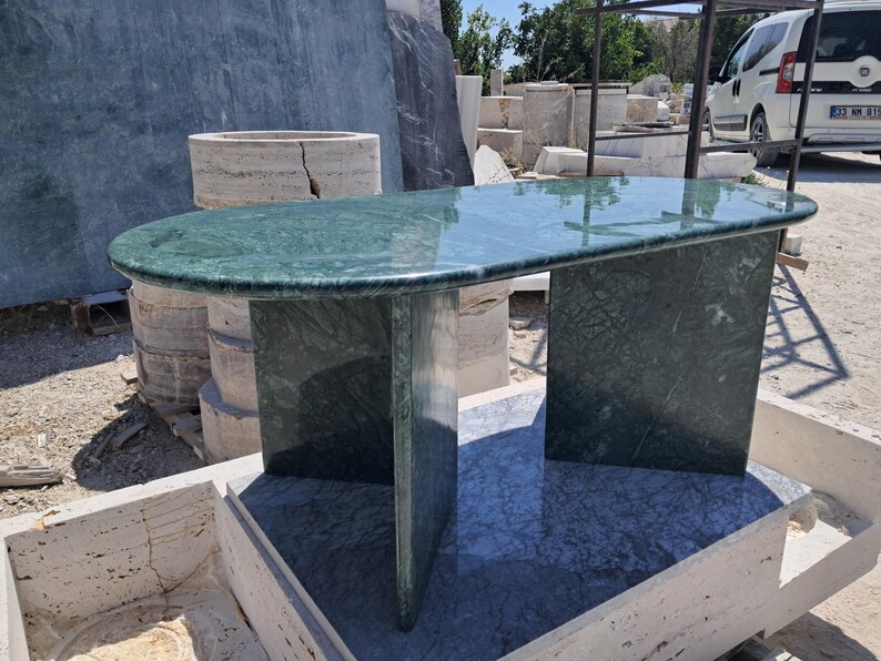 Puede incluir: Una mesa de m&aacute;rmol verde con una tapa ovalada y dos soportes rectangulares. La mesa tiene una superficie pulida y un patr&oacute;n de piedra natural. La mesa mide aproximadamente 152 cm de largo y 76 cm de ancho.
