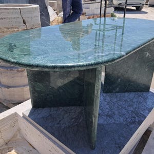 Puede incluir: Una mesa ovalada de m&aacute;rmol verde con superficie pulida. La mesa tiene una base s&oacute;lida con dos soportes rectangulares. La mesa mide aproximadamente 152 cm de largo y 76 cm de ancho.