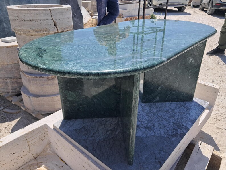 Puede incluir: Una mesa ovalada de m&aacute;rmol verde con superficie pulida. La mesa tiene una base s&oacute;lida con dos soportes rectangulares. La mesa mide aproximadamente 152 cm de largo y 76 cm de ancho.