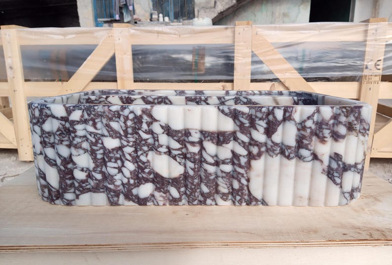 Puede incluir: Un lavabo rectangular de m&aacute;rmol con un dise&ntilde;o blanco y morado oscuro. El lavabo tiene un exterior estriado y est&aacute; colocado sobre una superficie de madera. El lavabo es un accesorio de ba&ntilde;o.