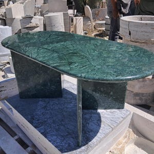 Puede incluir: Una mesa ovalada de m&aacute;rmol verde con un dise&ntilde;o &uacute;nico. La mesa tiene un color verde oscuro con vetas verdes m&aacute;s claras. La mesa est&aacute; sostenida por dos patas rectangulares y una pata central &uacute;nica. La mesa mide aproximadamente 152 cm de largo.
