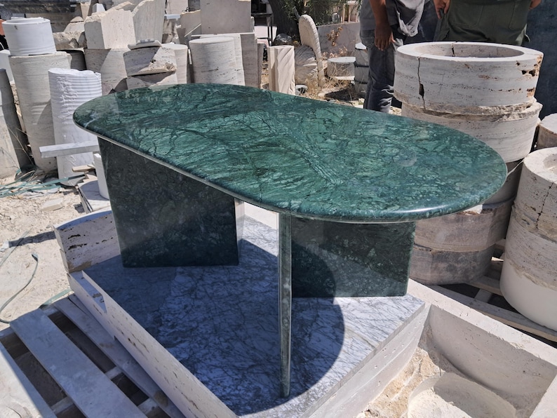 Puede incluir: Una mesa ovalada de m&aacute;rmol verde con un dise&ntilde;o &uacute;nico. La mesa tiene un color verde oscuro con vetas verdes m&aacute;s claras. La mesa est&aacute; sostenida por dos patas rectangulares y una pata central &uacute;nica. La mesa mide aproximadamente 152 cm de largo.