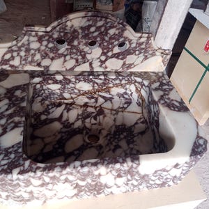 May include: A rectangular marble sink with a decorative backsplash. The sink features a white and burgundy patterned design. The backsplash has three faucet holes. The sink is made of stone and is likely for a bathroom.