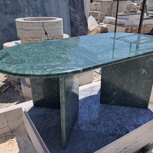 Puede incluir: Mesa de m&aacute;rmol verde con tapa rectangular redondeada y dos patas de soporte. La mesa tiene una superficie pulida y un patr&oacute;n de vetas natural. La mesa mide aproximadamente 152 cm de largo y 76 cm de ancho.