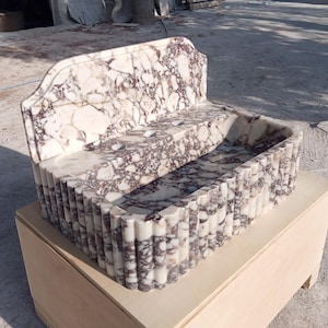 Könnte beinhalten: Ein Marmorwaschbecken mit dekorativer Rückseite und geriffelter Front. Das Waschbecken ist weiß mit burgunderfarbenen Adern und steht auf einem Holzsockel. Das Waschbecken ist für ein Badezimmer oder eine Gästetoilette konzipiert.