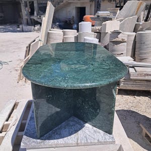 Puede incluir: Una mesa de m&aacute;rmol verde con una tapa rectangular redondeada y una base de pedestal. La mesa est&aacute; hecha de m&aacute;rmol verde pulido con vetas oscuras. La mesa mide aproximadamente 122 cm de largo y 61 cm de ancho.