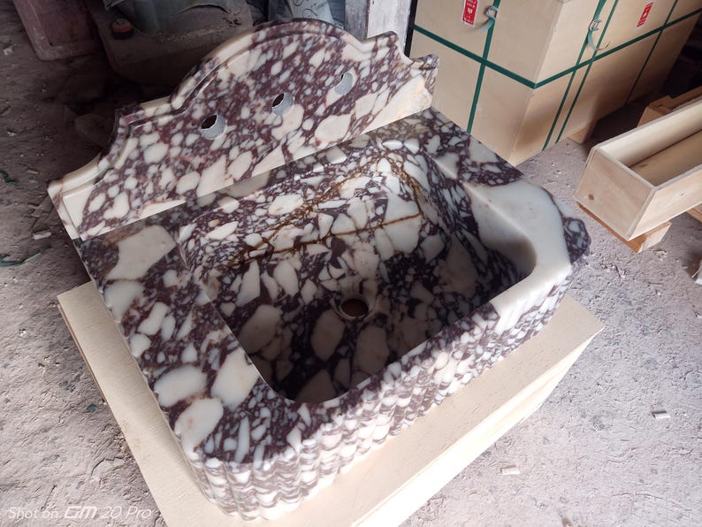May include: A marble sink with a decorative backsplash. The sink basin is rectangular with a rounded front edge. The marble has a white and burgundy pattern. The backsplash has two holes for faucets.