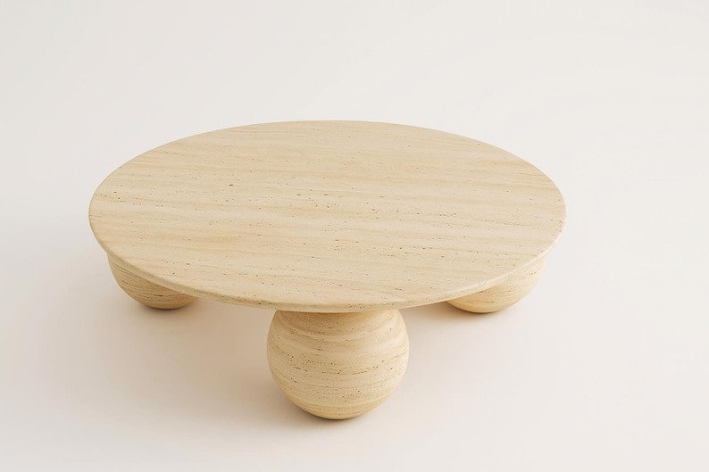May include: A round, light-colored coffee table with a natural wood grain finish. The table has a circular top and is supported by three spherical legs and a central, larger spherical base. The table is approximately 30 inches in diameter.