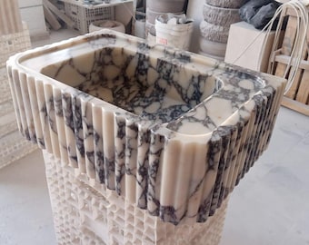 May include: A rectangular marble sink with a cream and gray veined pattern. The sink has a fluted edge and sits on a decorative base. The sink is a bathroom fixture.