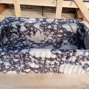 Puede incluir: Lavabo rectangular de m&aacute;rmol con un dise&ntilde;o blanco y morado oscuro. La pila tiene un exterior estriado y est&aacute; hecha de piedra natural. El lavabo es un elemento decorativo para un ba&ntilde;o.
