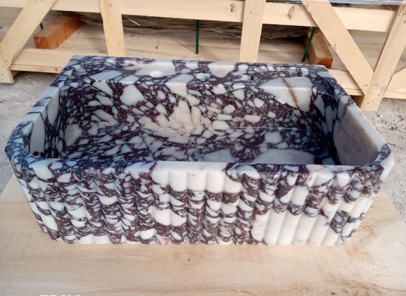 Puede incluir: Lavabo rectangular de m&aacute;rmol con un dise&ntilde;o blanco y morado oscuro. La pila tiene un exterior estriado y est&aacute; hecha de piedra natural. El lavabo es un elemento decorativo para un ba&ntilde;o.