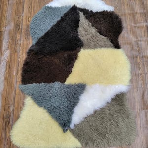 May include: A patchwork area rug constructed from multiple irregular sections of long-pile sheepskin. The rug features a color palette of cream, dark brown, sage green, slate gray, and white, arranged in a geometric, multi-textured composition.