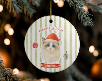 May include: Round Christmas ornament with a cat wearing a Santa hat, the text "Meowy Christmas" and "Fluffy". The ornament has a striped background with red and green accents. A gold string is attached for hanging.