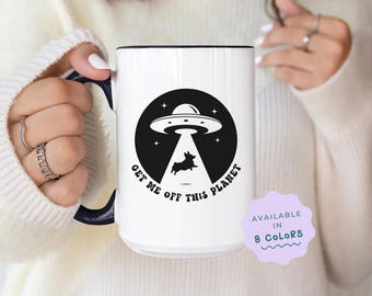 May include: White ceramic mug with a black and white graphic of a UFO and a dog with the text "Get me off this planet".