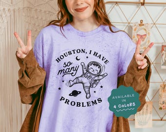 May include: Purple tie-dye t-shirt with a black and white illustration of a cat in a spacesuit. The text on the shirt reads "Houston, I have so many problems".