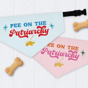 May include: Two dog bandanas, one light blue and one pink, with the phrase "PEE ON THE Patriarchy" in colorful text. Each bandana has a black adjustable strap and is accompanied by a bone-shaped dog treat.