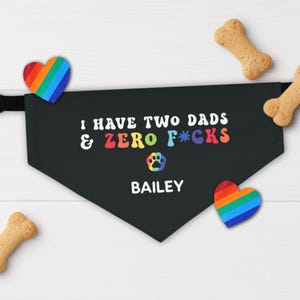 May include: Black dog bandana with the text "I HAVE TWO DADS & ZERO F*CKS" in rainbow colors, a paw print, and the name "BAILEY". Includes two rainbow heart-shaped decorations and three dog bone treats.