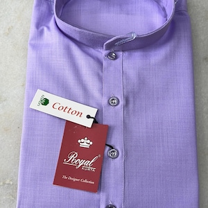 May include: A folded, pale purple cotton kurta shirt with a mandarin collar and button-down front. The shirt has a tag that reads "Royal Kurta" and "The Designer Collection". A smaller tag reads "Cotton".