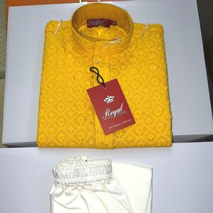 May include: A vibrant yellow kurta shirt with detailed embroidery, accompanied by cream-coloured trousers. The shirt has a mandarin collar and a "Royal Kurta" tag. The outfit is neatly folded, indicating formal attire. The measurements are in cm.