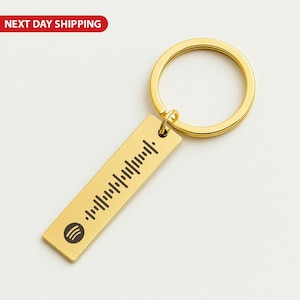 May include: A gold-coloured metal keyring with a rectangular tag featuring a Spotify code and logo. The keyring has a circular ring and a rectangular tag with a series of vertical lines. The words "NEXT DAY SHIPPING" are in a red oval in the top left corner.