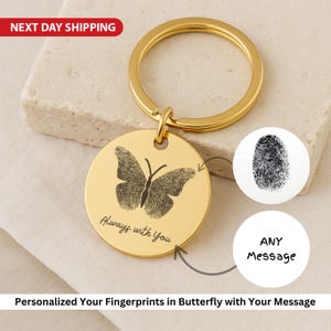 Op de afbeelding: Goudkleurige sleutelhanger met een ronde hanger met een vlinderprint gemaakt van een vingerafdruk. De hanger heeft de inscriptie "Always with You". Inclusief een vingerafdruk-afbeelding en ruimte voor een aangepaste boodschap.