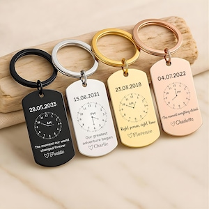May include: Four rectangular metal keychains in black, silver, gold, and rose gold finishes. Each features a circular ring, a clock face graphic with specific dates, times, and engraved text including names like Freddie, Charlie, Florence, and Charlotte.