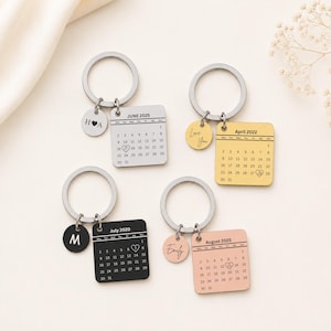 May include: Four metal keychains featuring square calendar charms and small circular tags. The calendars show June 2025, April 2022, July 2020, and August 2025 with specific dates circled by hearts. The circular tags are engraved with H A, Love You, M, and Emily.