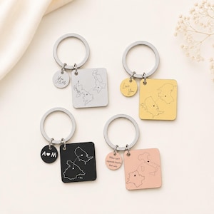 May include: Four metal keychains with square pendants featuring engraved maps connected by a dotted line and small heart icons. Each keychain includes a circular charm with text: You & Me, Love You, A heart M, and Miles can't separate hearts that care.