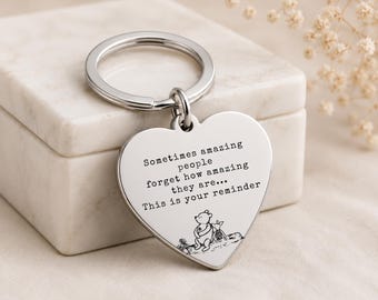 May include: A silver-toned heart-shaped keychain featuring an engraved quote that reads: Sometimes amazing people forget how amazing they are... This is your reminder. Below the text is a small black line drawing of Winnie the Pooh and Piglet.