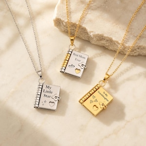 Op de afbeelding: Drie metalen kettingen met hangers in de vorm van miniatuurboeken. Eén zilverkleurige hanger heeft de tekst 'My Little Star', één goudkleurige 'Best Mom Ever' en één 'To My Granddaughter', allemaal voorzien van kleine gegraveerde hartjes.