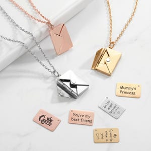 May include: Necklaces with envelope pendants in silver, rose gold, and gold. Some pendants are open, revealing a small compartment. Included are small rectangular tags with engraved phrases like "Queen" and "You're my best friend."