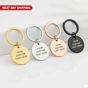 Könnte beinhalten: Vier Schlüsselanhänger mit runden Anhängern, jeweils mit dem Text "YOUR CUSTOM TEXT HERE". Die Schlüsselanhänger sind in Gold, Silber, Roségold und Schwarz erhältlich. Das Bild enthält ein rotes Banner mit der Aufschrift "NEXT DAY SHIPPING."