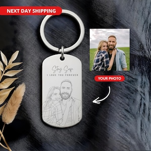 Op de afbeelding: Zilverkleurige metalen sleutelhanger met een rechthoekig label. Het label heeft een lijntekening van een stel en de tekst "Stay Safe I Love You Forever". Een kleine foto van het stel is ook inbegrepen. De sleutelhanger heeft een ronde ring.