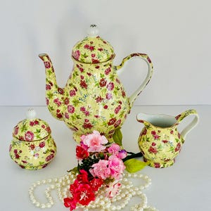 May include: A yellow and pink floral tea set with a teapot, creamer, and sugar bowl. The set is made of porcelain and has a delicate floral pattern.