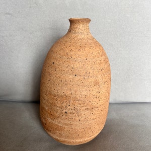 Puede incluir: Un jarrón de cerámica marrón moteado con cuerpo redondeado y cuello estrecho.