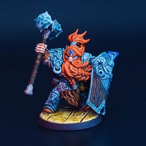 May include: A miniature fantasy figure of a dwarf warrior, wielding a large blue and silver war hammer and shield. The dwarf has a long, orange beard and is clad in detailed armor. The figure is posed on a circular base with a tiled floor design.