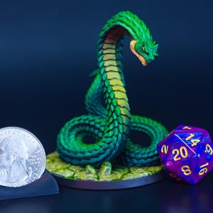 May include: A detailed miniature of a green and yellow serpent with a red mouth, with a coin and a twenty-sided die. The serpent is likely for tabletop gaming. The coin is for scale.