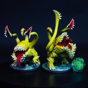 May include: Two painted miniature monster figures featuring yellow, textured bodies with large, open mouths, sharp white teeth, and red tongues. Each creature has multiple tentacle-like appendages with smaller mouths, standing on circular bases.