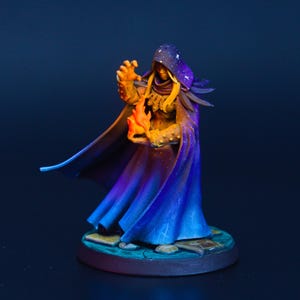 May include: A miniature fantasy figure of a robed sorcerer, holding a flame. The figure is painted with vibrant colors, including blues, purples, and gold. The sorcerer wears a starry hood and a long flowing cloak. The base is a circular platform.